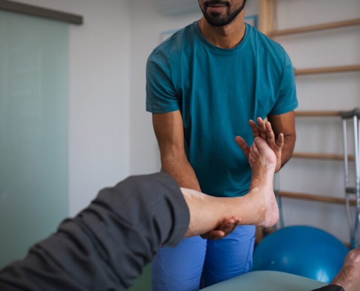 A close-up of physiotherapist exercising with senior patient's leg in a physic room.